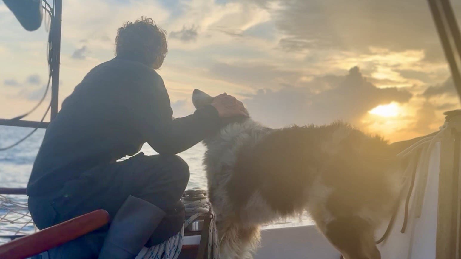 Captain Kimmer petting Casper the sailing dog on a sailboat at sunset in the Atlantic